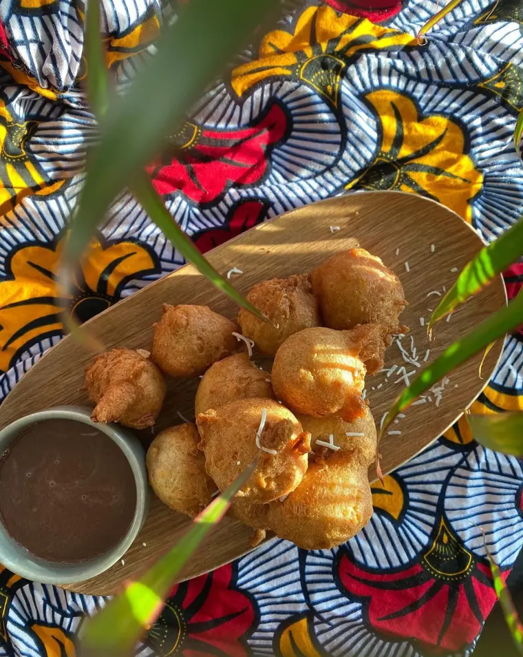 Accras dorés servis sur une planche en bois avec sauce, sur tissu wax